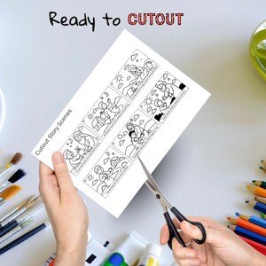 Puede incluir: Una hoja de papel blanca con ilustraciones en blanco y negro de Cutout Story Scenes se est&aacute; cortando con tijeras. El texto "Ready to CUTOUT" est&aacute; en la parte superior. Pinceles, tubos de pintura y l&aacute;pices de colores est&aacute;n en el fondo.