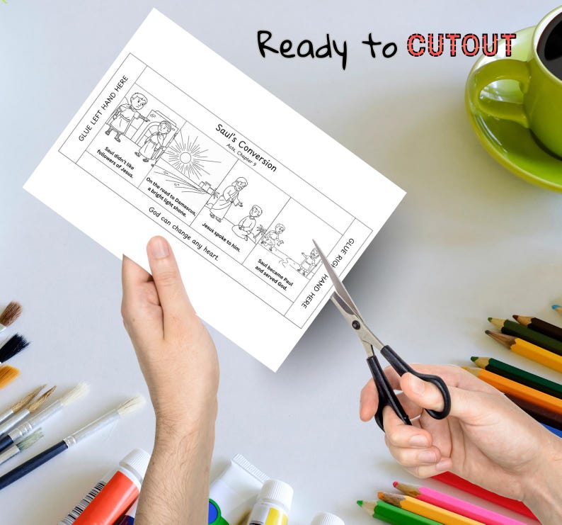 May include: A black and white illustrated cutout sheet with the text "Saul's Conversion" and "Ready to CUTOUT". The sheet is being cut with scissors. A green mug and colored pencils are in the background.