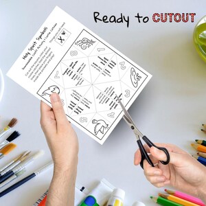 May include: A white paper with the text "Holy Spirit Symbols" and instructions for a craft activity. The paper is being cut with scissors. The words "Ready to CUTOUT" are written at the top.