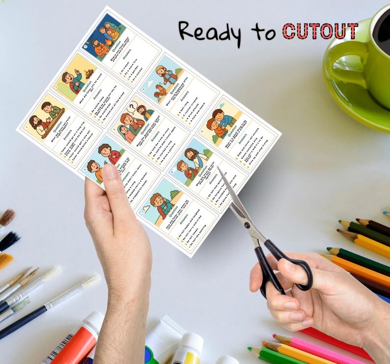 May include: A sheet of illustrated cards with questions and answers, held by a person's hand, being cut with scissors. The cards feature colorful cartoon images and text. The words "Ready to Cutout" are printed at the top.