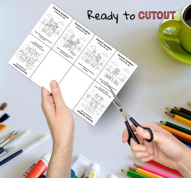 May include: A sheet of paper with black and white illustrations and text, including the words "David & Jonathan" and "Ready to CUTOUT." Scissors are cutting the paper. Colored pencils and paint tubes are in the background.