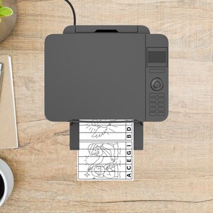 May include: A gray printer is printing a black and white image of a religious scene. The image is a puzzle with the letters ACEGIBD printed on the side. The printer is on a wooden surface.