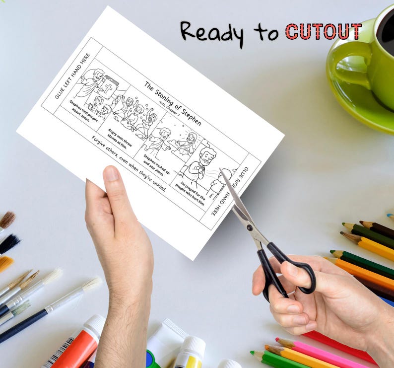 May include: A black and white illustrated paper with the text "The Stoning of Stephen" and "Ready to CUTOUT". The paper is being cut with scissors. A green mug and colored pencils are in the background.