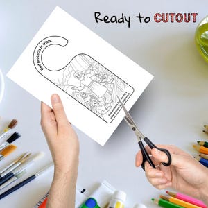 May include: A white door hanger with a black and white illustration of a biblical scene. The text "God protects in trials" and "God protects Paul during a violent storm and shipwreck" are visible. Scissors are cutting the door hanger.