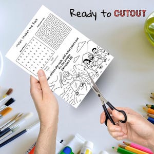 May include: A black and white activity sheet with the text "Moses Strikes the Rock" is being cut with scissors. The sheet includes a word search, a maze, and an illustration of Moses striking a rock. The words "Ready to CUTOUT" are written at the top.