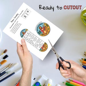May include: A white paper with the text "Palm Sunday" and illustrations is being cut with scissors. The paper includes instructions and a circular image. The words "Ready to CUTOUT" are at the top.