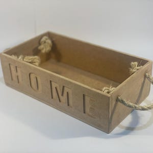 May include: A rectangular wooden box with the word "HOME" cut out on the front. The box has rope handles on each end. The box is made of light brown wood and is empty.