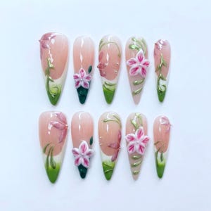 May include: Set of ten almond-shaped artificial nails. Each nail features a pink and white gradient design, with painted pink flowers, green vines, and 3D pink flowers. The nails have a glossy finish.