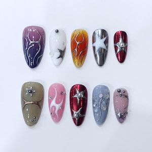 May include: A set of ten artificial nails in various colors and designs. The nails feature a range of colors, including purple, white, orange, silver, and red. Designs include stars, flames, and abstract silver lines.