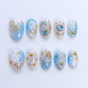 May include: A set of ten artificial nails with a winter theme. Each nail features a light blue and white base with gold and silver accents. Designs include snowflakes, stars, hearts, and swirls. The nails are oval-shaped and have a glossy finish.