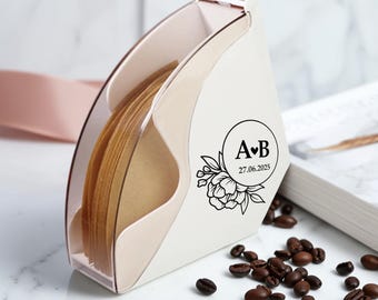 May include: A white coffee filter holder with a clear plastic front, holding brown paper filters. The holder has a decorative black floral design with the initials "A♥B" and the date "27.06.2025". Coffee beans are scattered around the holder.