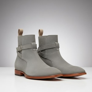May include: A pair of gray suede ankle boots with a strap and buckle detail. The boots have a rounded toe and a pull tab at the back. The soles are brown.