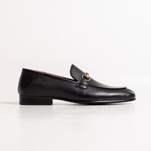 May include: Black leather loafers with a gold chain detail. The loafers have a pointed toe and a low heel.