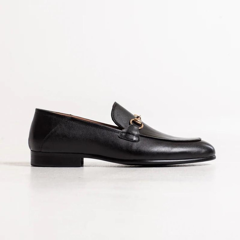 May include: Black leather loafers with a gold chain detail. The loafers have a pointed toe and a low heel.