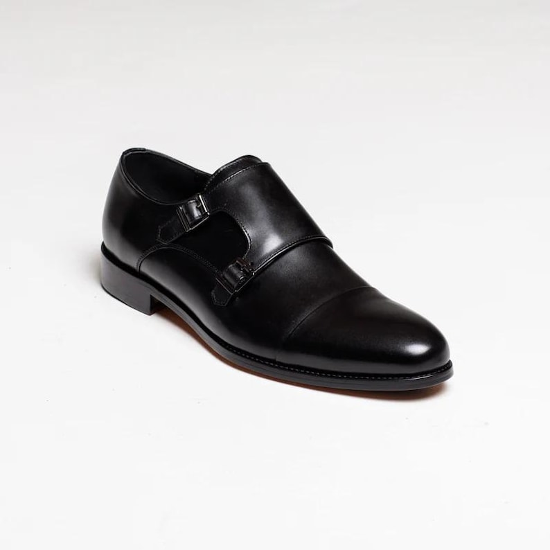 Puede incluir: Zapatos de vestir de cuero negro con doble hebilla monje y punta puntiaguda.