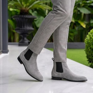 Peut inclure: Bottes Chelsea en daim gris avec des empiècements latéraux élastiques noirs et des semelles noires. Les bottes sont portées avec un pantalon à carreaux gris. Chaussures élégantes.