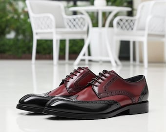 May include: Two-tone leather dress shoes with a burgundy upper and black toe and heel. The shoes feature a wingtip design with decorative perforations and black laces. The shoes are suitable for formal occasions.