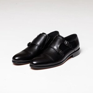 Puede incluir: Un par de zapatos de vestir de cuero negro con doble hebilla monje. Los zapatos tienen un dise&ntilde;o cl&aacute;sico con punta puntiaguda y cierre de hebilla.