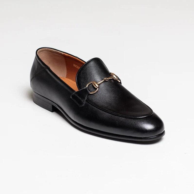 May include: Black leather loafers with a gold metal buckle detail.