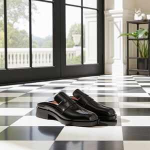 Könnte beinhalten: Ein Paar schwarze Leder-Slipper mit niedrigem Absatz. Die Schuhe haben eine glänzende Oberfläche und einen Riemen über dem Oberteil. Sie stehen auf einem schwarz-weiß karierten Boden, mit Blick auf ein Fenster und einen Garten im Hintergrund.
