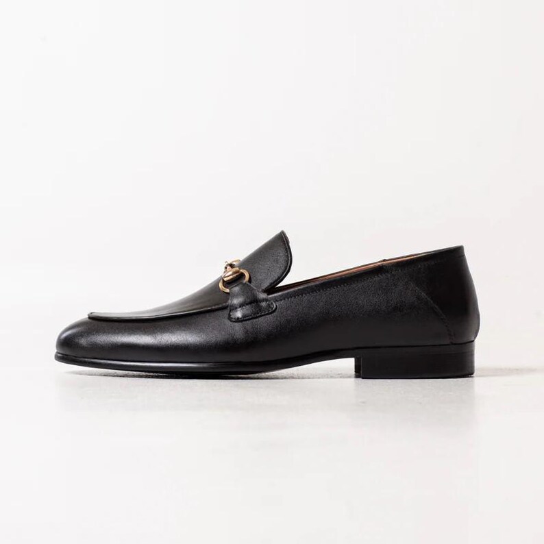 May include: Black leather loafers with a gold chain detail.