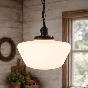 May include: A white glass pendant light suspended from a black chain in a rustic kitchen setting. The light fixture is the central element, brightening the area. A wooden table, flowers, and a farmhouse sink are also present.