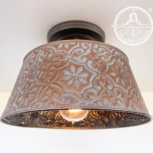 May include: A ceiling light fixture with a distressed copper and white metal shade featuring a decorative embossed pattern. The shade is round and has a slight curve to it. The light fixture is mounted to a white ceiling.