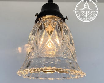 May include: Clear glass pendant light with a diamond pattern shade and a black metal fixture. The light fixture is suspended from a black cord. The Lamp Goods logo is in the upper right corner.