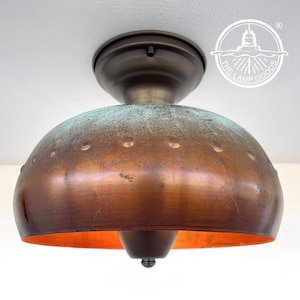May include: A copper ceiling light fitting with a domed shade and a distressed finish. The shade has a subtle green patina and is accented with small rivets. The fitting has a bronze finish.