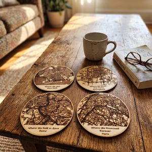 Pode incluir: Quatro porta-copos circulares de madeira com mapas de ruas gravados a laser. Cada porta-copos inclui texto: Where We Met New York, Where We Built the Home Springfield, Where We Fell in Love Rome e Where We Promised Forever Paris.