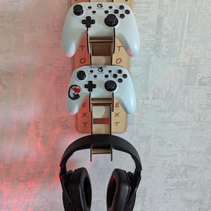 May include: A wooden gaming controller and headset holder. Two white game controllers are mounted on the holder, with a black headset below. The holder has the word "TEXT" on it.