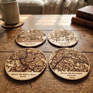 May include: Four round wooden coasters featuring laser-engraved city street maps. Each coaster includes text: Where We Met New York, Where We Built the Home Springfield, Where We Fell in love Rome, and Where We Promised Forever Paris.