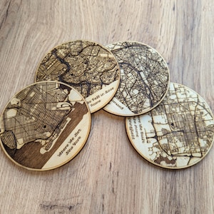 Può includere: Quattro sottobicchieri rotondi in legno con mappe di città incise. Uno dice "Where We Met New York", un altro "Be Fell in Love Rome", e un terzo "Where We Built the Home Springfield". I sottobicchieri sono in legno chiaro.