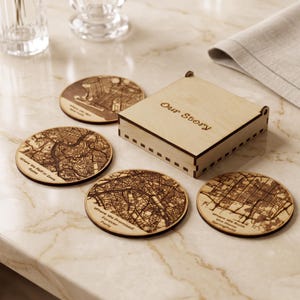May include: A set of four circular wooden coasters featuring laser-engraved city maps and text, accompanied by a square wooden storage box with the words "Our Story" engraved on the lid. Each coaster displays a unique map design.