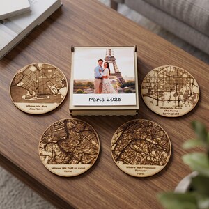 May include: A wooden box with a photo of a couple in front of the Eiffel Tower labeled Paris 2023, surrounded by four circular wooden coasters engraved with city maps and text reading Where We Met New York, Where We Built the Home Springfield, Where We Fell in Love Rome, and Where We Promised Forever Paris.