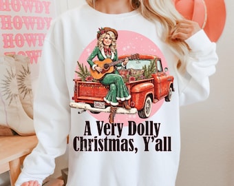 May include: White sweatshirt featuring a graphic of a woman playing a guitar in the back of a red truck. The graphic includes the text "A Very Dolly Christmas, Y'all". The background has a pink circle with snowflakes.