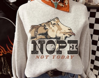 May include: A light gray sweatshirt featuring a graphic of a goat with its tongue out. The word "NOPE" is printed above "NOT TODAY" in a distressed font. The sweatshirt is styled with a bandana and necklace.