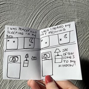 May include: A small, hand-drawn comic strip in black ink on white paper. The comic depicts a person in bed, with text bubbles describing a cat's meowing. The text includes "I was peacefully sleeping in my bed" and "When I heard my cat meowing."