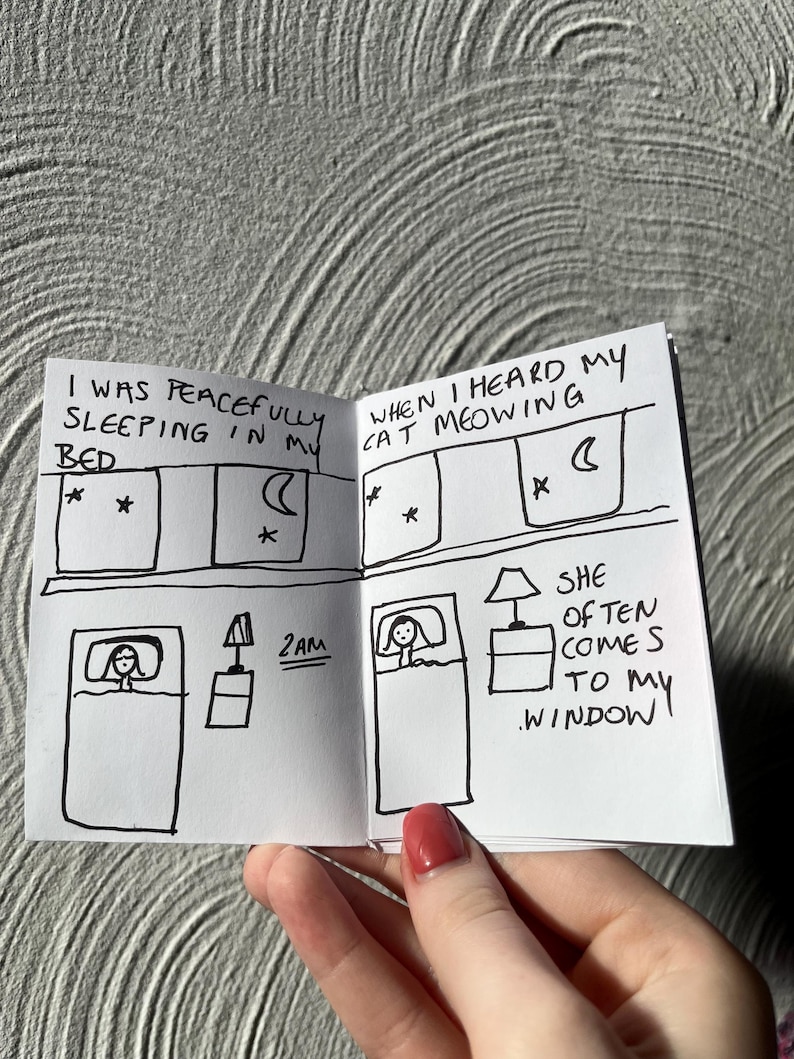 May include: A small, hand-drawn comic strip in black ink on white paper. The comic depicts a person in bed, with text bubbles describing a cat's meowing. The text includes "I was peacefully sleeping in my bed" and "When I heard my cat meowing."