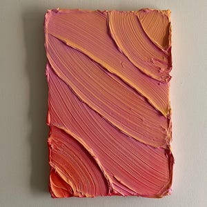 Op de afbeelding: Abstract kunstwerk met dikke, getextureerde penseelstreken in tinten roze, koraal en oranje. Het rechthoekige kunstwerk heeft diagonale streken, waardoor een gevoel van beweging en diepte ontstaat. De randen van het schilderij zijn ruw.