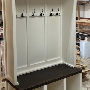May include: White wooden entryway bench with a dark brown top, three cubbies, and five hooks.