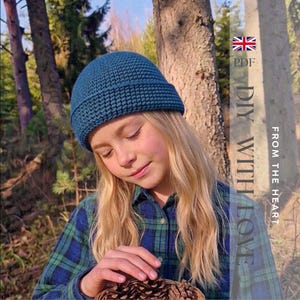 Peut inclure: Un bonnet en crochet bleu sarcelle avec un bord replié épais. Le texte sur le côté droit de l'image indique : PDF DIY WITH LOVE FROM THE HEART, accompagné d'une petite icône de drapeau du Royaume-Uni. Le bonnet présente un motif en maille dense.