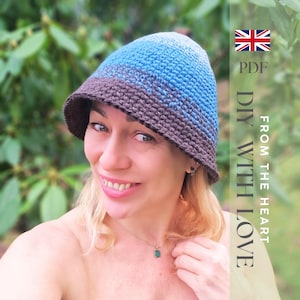 Peut inclure: Un chapeau seau crocheté bleu et marron avec un large bord. Le chapeau est fait à la main et a une finition texturée. L'image comprend le texte "DIY WITH LOVE" et un drapeau britannique.