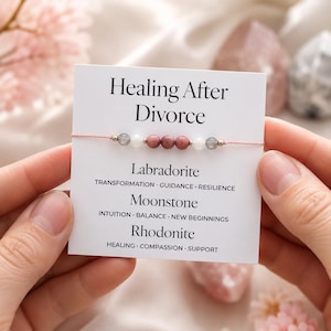 May include: A delicate bracelet with pink beads and a card that reads "Healing After Divorce." The card lists Labradorite, Moonstone, and Rhodonite, with associated keywords. The bracelet is held against a soft, blurred background.