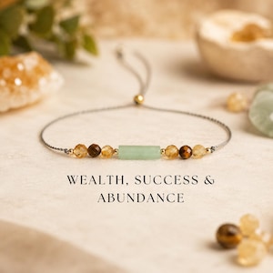 Può includere: Braccialetto regolabile con una pietra rettangolare verde chiaro, perline marroni e gialle e dettagli dorati. Il braccialetto è infilato su un cordoncino grigio. Il testo sull'immagine recita: WEALTH, SUCCESS & ABUNDANCE.