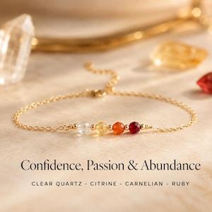 May include: A delicate gold chain bracelet featuring clear quartz, citrine, carnelian, and ruby gemstones. The bracelet is displayed on a neutral surface with the text "Confidence, Passion & Abundance".