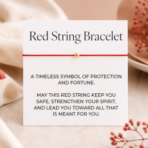 Può includere: Un braccialetto con filo rosso e perla dorata, esposto su un cartoncino bianco. Il cartoncino riporta "Red String Bracelet" e include testo su protezione e fortuna. Un design semplice ed elegante.