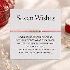 Op de afbeelding: Een rood touw armband met zeven goudkleurige kralen, gepresenteerd op een witte kaart. De kaart leest "Seven Wishes" en bevat tekst over het stellen van intenties. De armband is een eenvoudig, elegant accessoire.