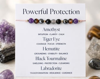 May include: A beaded bracelet with amethyst, tiger eye, hematite, black tourmaline, and labradorite stones. The bracelet is strung on a pink cord and displayed with a card that reads "Powerful Protection."