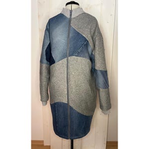 Könnte beinhalten: Eine lange Patchwork-Jacke mit Reißverschluss. Die Jacke hat eine Kombination aus Denim- und grauen Stoffbahnen. Die Ärmel und der Kragen sind grau, während der Körper Denim in verschiedenen Blautönen enthält. Die Jacke wird auf einer Schaufensterpuppe präsentiert.